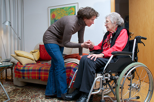 Tochter hält alter Mutter, die im Rollstuhl sitzt, die Hand
